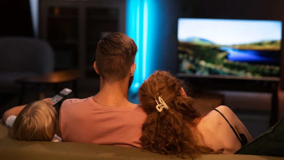 Zadní pohled na tříčlennou rodinu sledující TV v pozadí