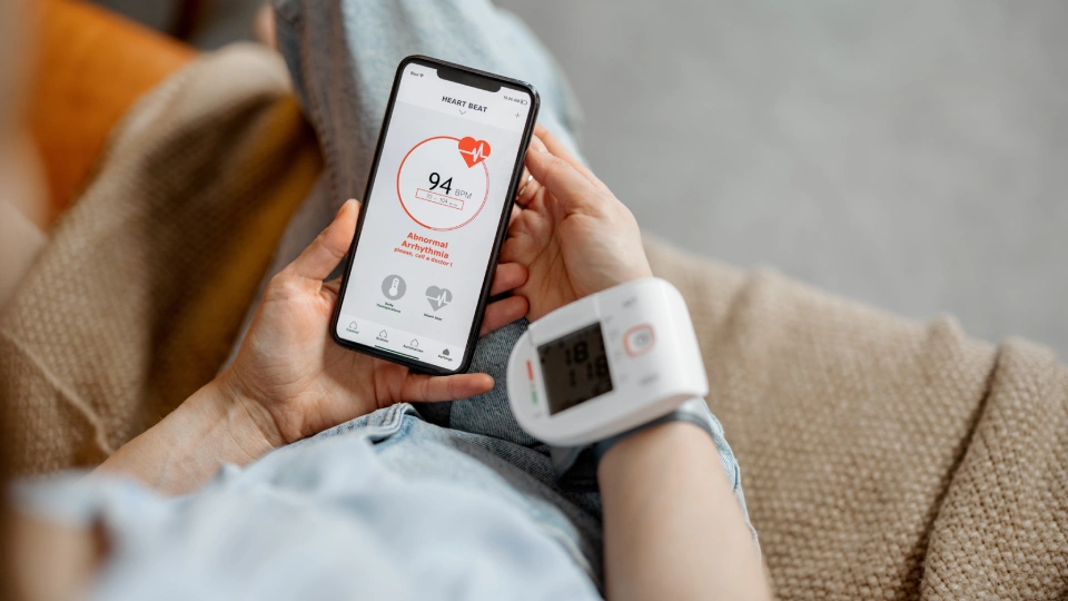 Pohled přes rameno ženy, která si měří tlak pomocí chytrého tlakoměru připojeného k mobilnímu telefonu