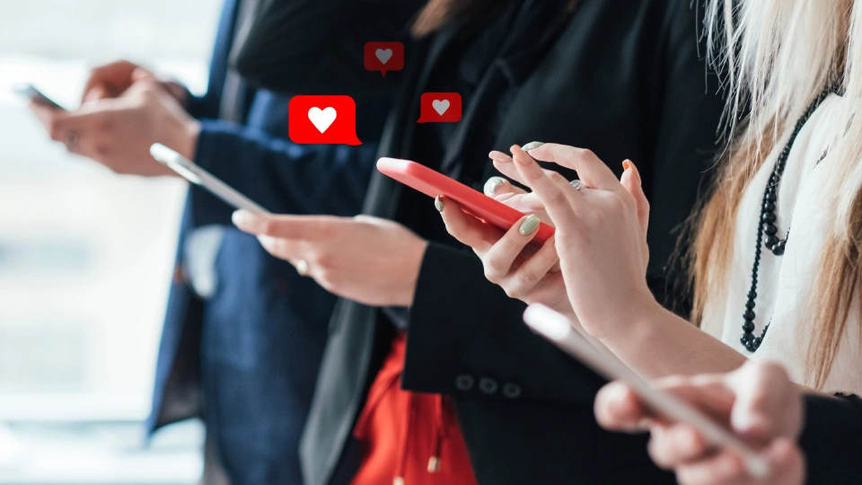 Boční detail na řadu rukou držících mobilní telefony, ze kterých stoupají ikonky srdíček