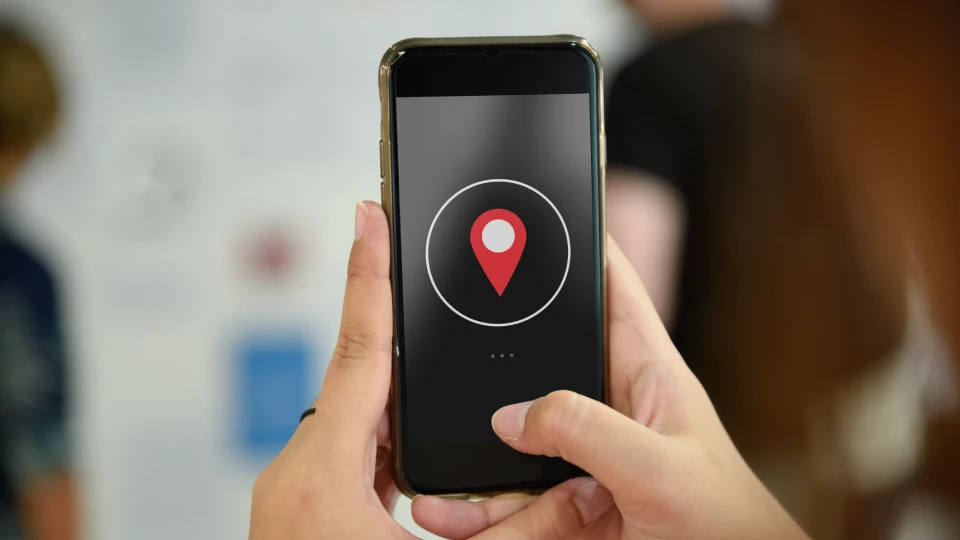 Detail na ruce držící mobilní telefon, na obrazovce se zobrazuje špendlík polohy